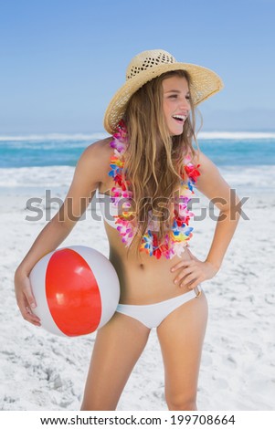 Fit smiling blonde in white bikini and straw hat holding beach ball on a sunny day