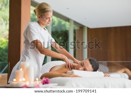 Smiling brunette getting a shoulder massage at the health spa