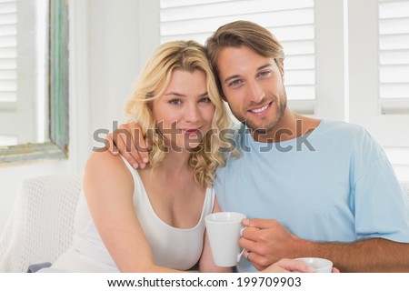 Couple having coffee on the couch smiling at camera at home in the living room