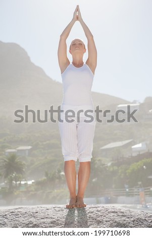 Blonde woman standing in tree pose on beach on a sunny day