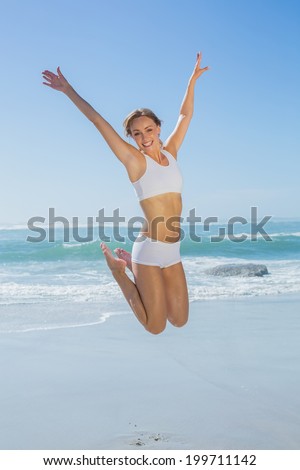 Gorgeous fit blonde jumping by the sea with arms out on a sunny day