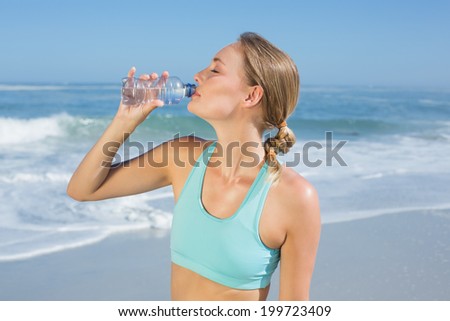 Fit woman standing on the beach taking a drink on a sunny day