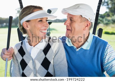 Happy golfing couple sitting in golf buggy smiling at each other on a sunny day at the golf course