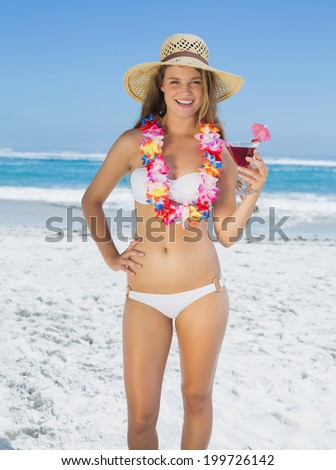 Pretty smiling blonde in floral garland holding cocktail on the beach on a sunny day