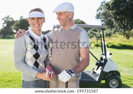 Happy golfing couple with golf buggy behind on a sunny day at the golf course