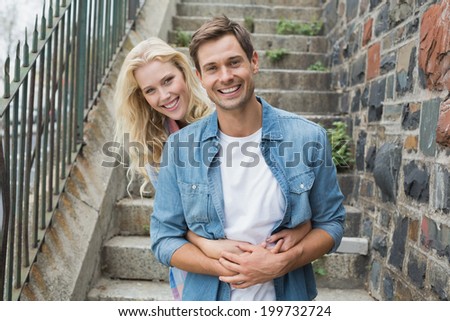 Hip young couple sitting on steps smiling at camera on a sunny day in the city