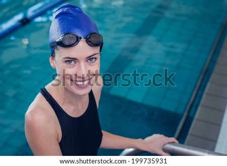Fit swimmer smiling at camera getting out of the swimming pool at the leisure center