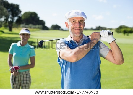 Happy golfer teeing off with partner behind him on a sunny day at the golf course