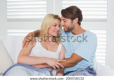 Cute casual couple sitting on couch under blanket at home in the living room