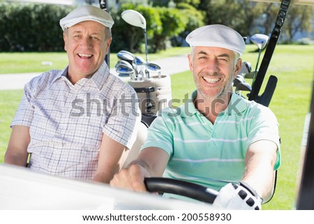 Golfing friends driving in their golf buggy smiling at camera on a sunny day at the golf course