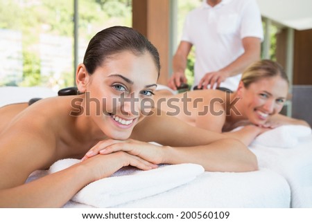 Pretty friends lying on massage tables with hot stones on their backs in the health spa