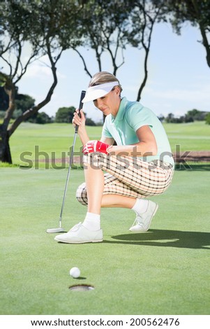 Female golfer watching her ball on putting green on a sunny day at the golf course