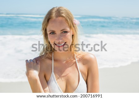 Beautiful blonde in white bikini smiling at camera on the beach on a sunny day