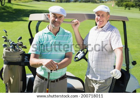 Golfing friends standing beside their buggy smiling at camera on a sunny day at the golf course