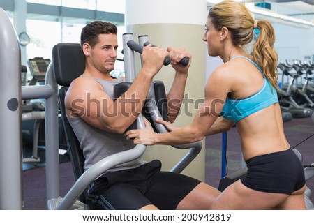 Personal trainer coaching bodybuilder using weight machine at the gym