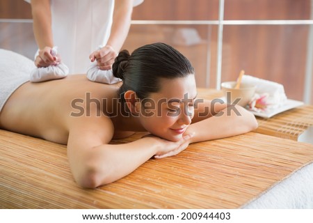 Smiling brunette getting a herbal compress massage at the health spa
