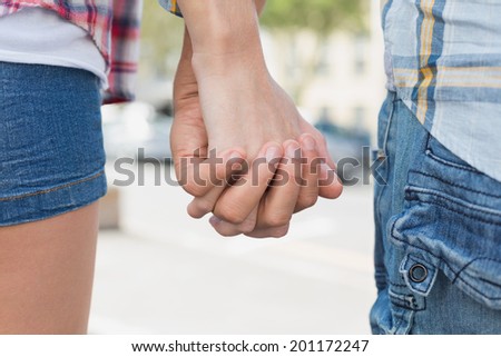 Couple in check shirts and denim holding hands on a sunny day in the city