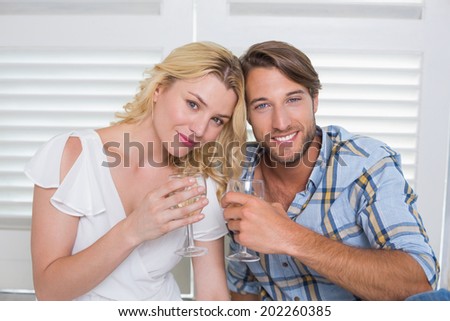 Cute young couple sitting on floor together having white wine at home in the living room