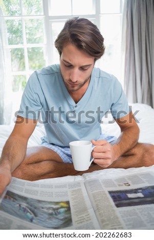 Handsome man sitting on bed reading the paper with coffee at home in the living room