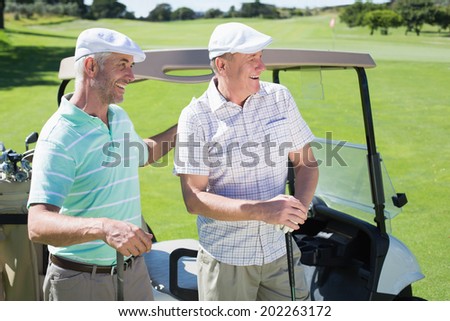 Golfing friends standing beside their buggy smiling on a sunny day at the golf course