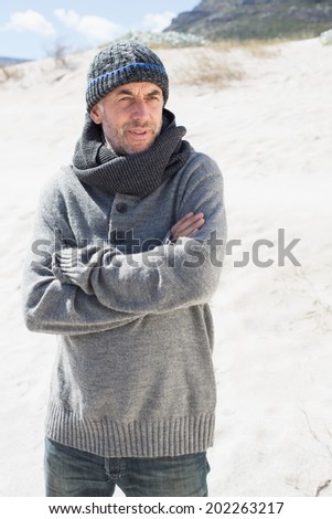 Attractive man shivering on the beach in hat and scarf on a bright but cool day