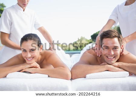 Smiling couple enjoying couples massage poolside outside at the spa