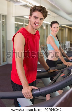Smilng man and woman on the treadmills at the gym