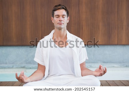 Handsome man in white meditating in lotus pose in health spa