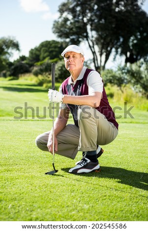 Golfer kneeling holding his golf club on a sunny day at the golf course