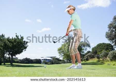 Female concentrating golfer teeing off on a sunny day at the golf course
