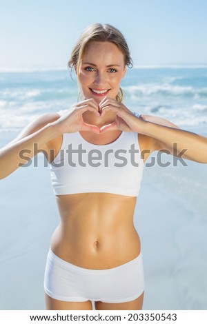 Gorgeous fit blonde making heart shape with hands by the sea on a sunny day
