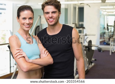 Fit man and woman smiling at camera together at the gym