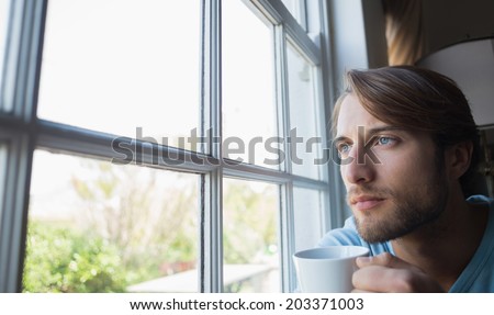 Thoughtful man looking out the window at home in the living room