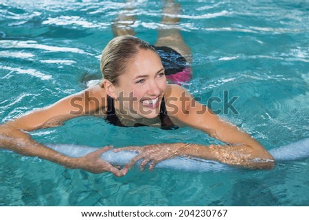 Fit blonde swimming with foam roller in swimming pool at the leisure centre