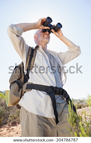 Hiker standing on country trail looking through binoculars on a sunny day