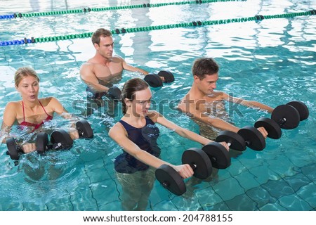 Happy fitness class doing aqua aerobics with foam dumbbells in swimming pool at the leisure centre
