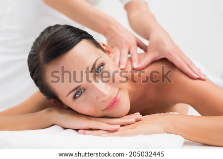 Beautiful brunette enjoying a shoulder massage smiling at camera in the health spa
