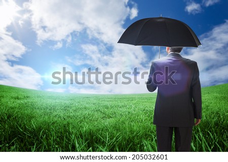 Mature businessman holding an umbrella against green field under blue sky