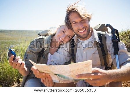 Hiking couple taking a break on mountain terrain using map and compass on a sunny day