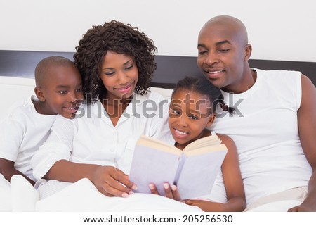 Happy family reading book together in bed at home in the bedroom
