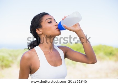 Fit woman drinking water from sports bottle on a sunny day in the countryside