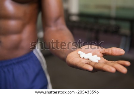 Close-up mid section of muscular man holding vitamin pills in hand