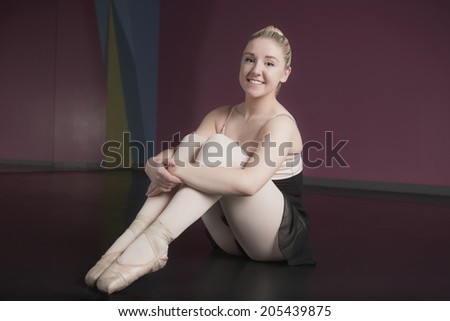 Pretty ballerina sitting and smiling at camera in the ballet studio