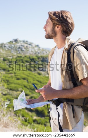 Handsome hiker holding map and compass at mountain summit on a sunny day