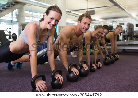 Fitness class in plank position with kettlebells at the gym