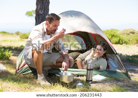 Outdoorsy couple cooking on camping stove outside tent on a sunny day