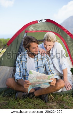 Attractive happy couple sitting by their tent reading map on a sunny day