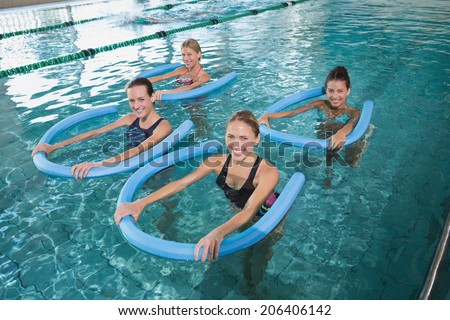 Fitness class doing aqua aerobics with foam rollers in swimming pool at the leisure centre