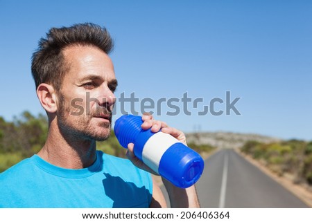 Athletic man on open road taking a drink on a sunny day