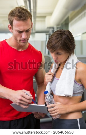 Handsome personal trainer with his client looking at clipboard at the gym